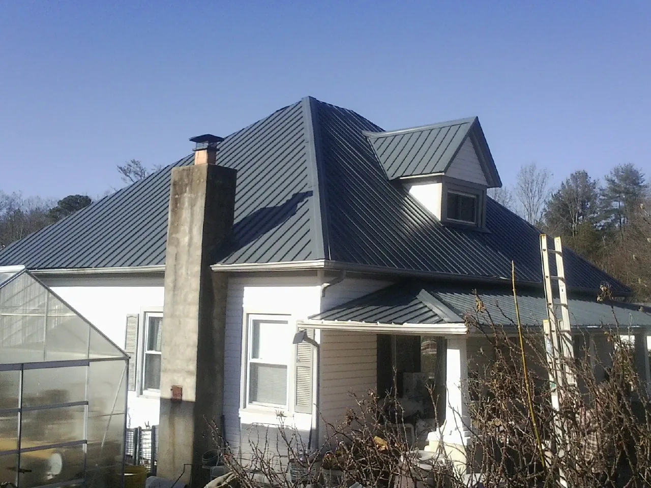 Dark blue standing seam metal roof on a white farmhouse with dormer — Slate & Tile Roof Repair by Roofing Brothers in Ellinwood