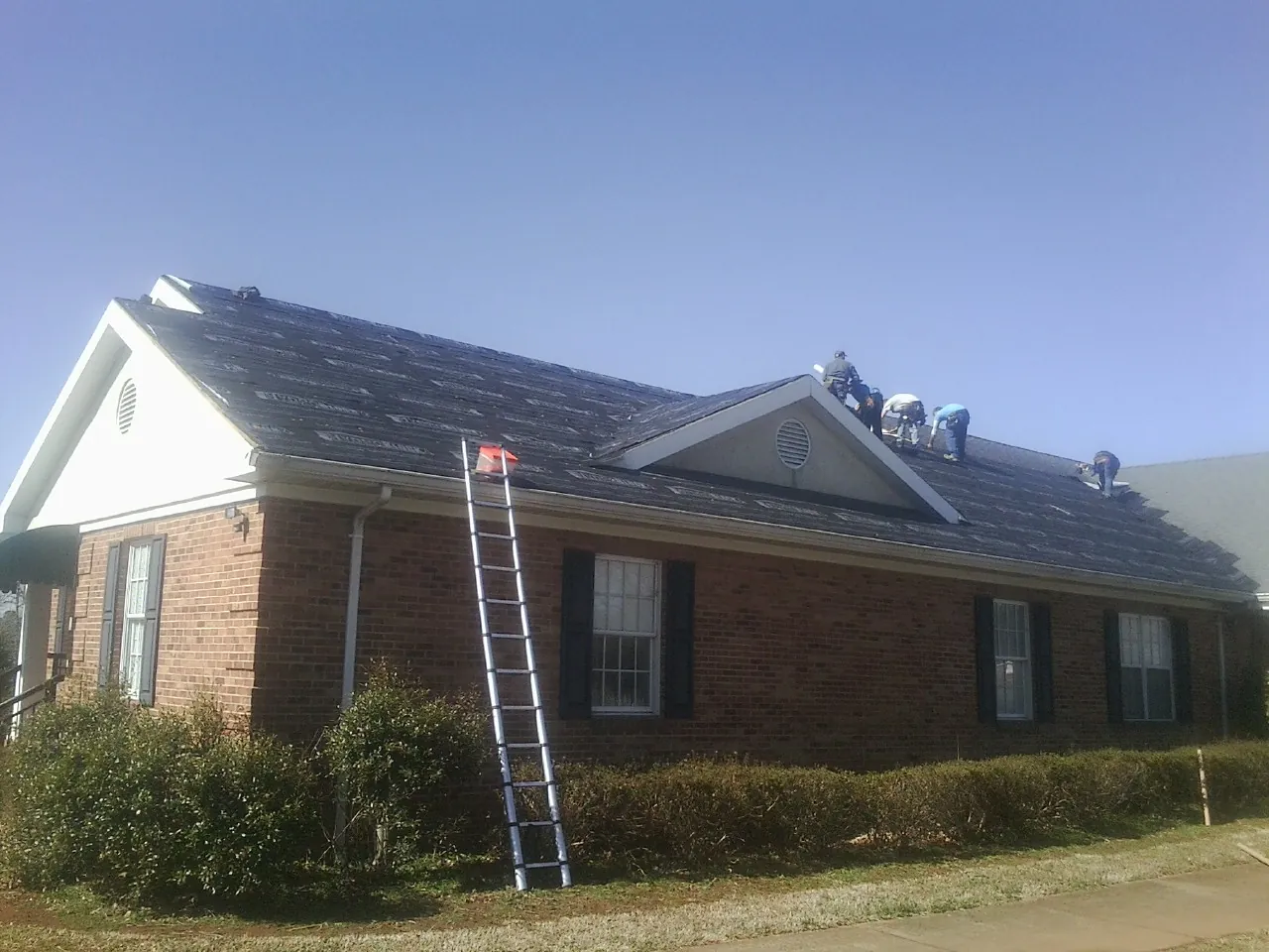Crew tearing shingles off a brick ranch roof with a ladder set — Emergency Roof Repair work by our crew in Ellinwood