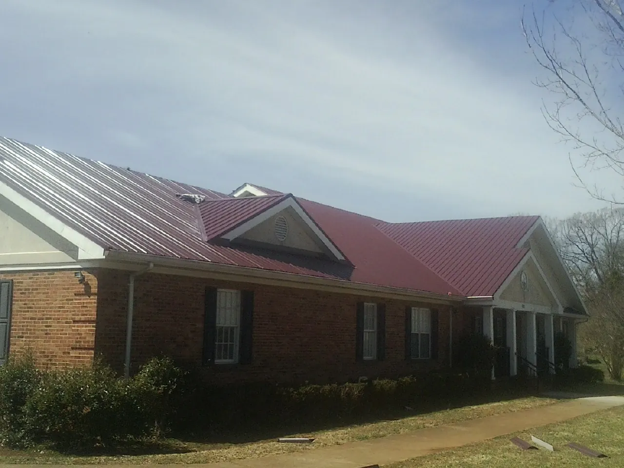 Red metal roof with gabled entries on a long brick building, from a Hail Damage Roof Repair job in Ellinwood