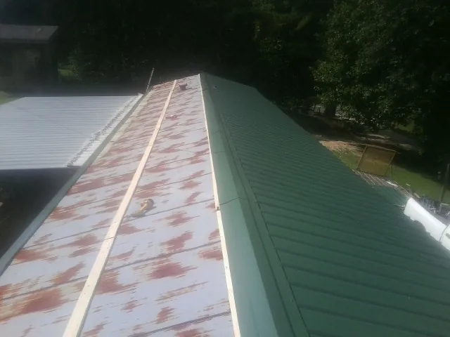 Old rusted panels beside newly installed green metal roofing — Wind Damage Roof Repair by Roofing Brothers in Ellinwood