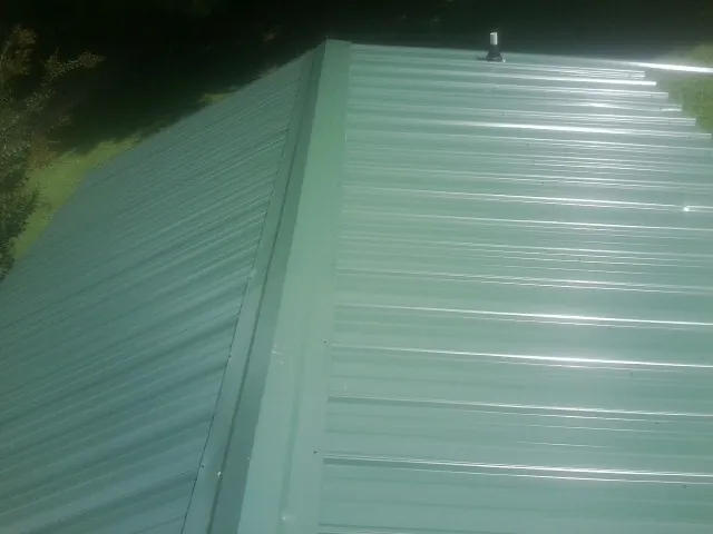 New green metal panels meeting at the ridge of a roof — Flat Roof Repair work by our crew in Ellinwood