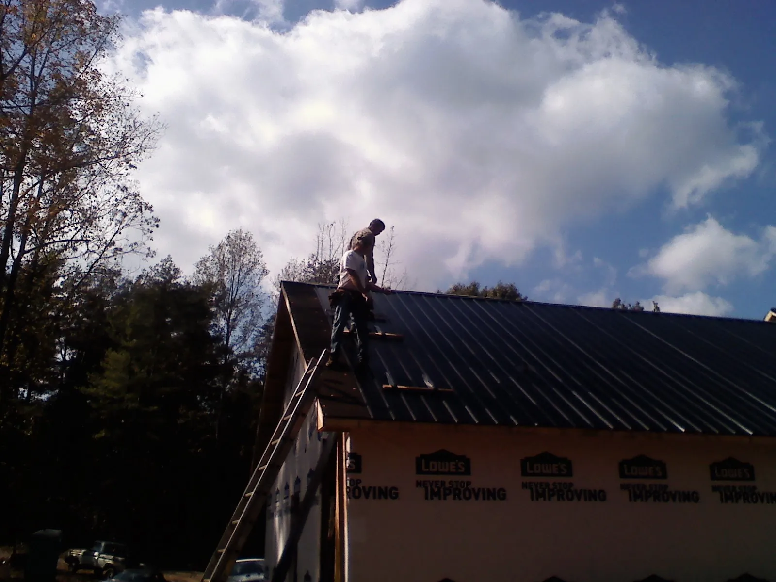 Roofer fastening dark metal panels high against a cloudy sky, from a Roof Inspection job in Ellinwood