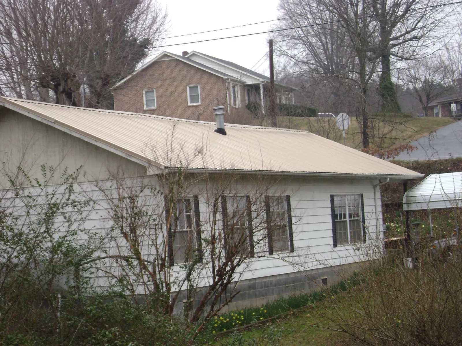 Tan metal roof on a white sided house set into a hillside — Commercial Roofing by Roofing Brothers in Ellinwood