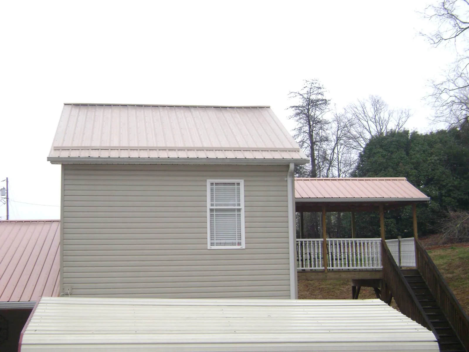 Tan metal roofs on a two story addition and attached porch, from a Roof Replacement job in Ellinwood