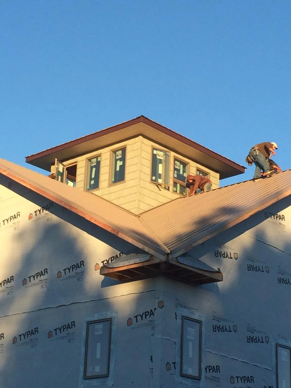 Roofers working around a rooftop cupola on a new metal roof at sunset — Roof Waterproofing in Ellinwood by Roofing Brothers